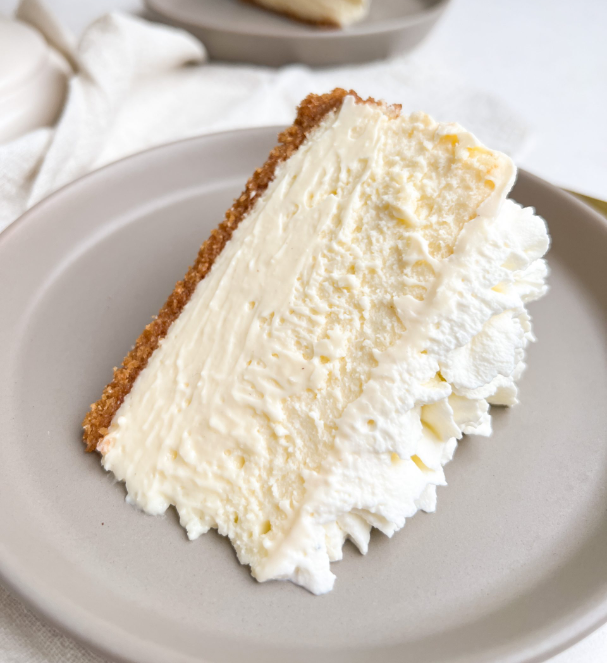 Close-up of a slice of cheesecake on a small plate, showcasing a thin crust, a smooth and creamy texture, and a dollop of whipped cream on top.