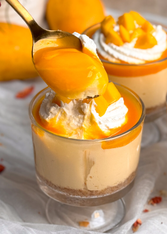 A spoon poised above a no bake mango cheesecake dessert cup, showcasing a generous bite.