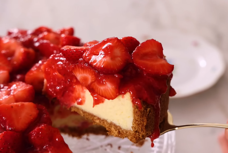 A slice of strawberry cheesecake on a small round plate, topped with strawberry compote and revealing a creamy center.






