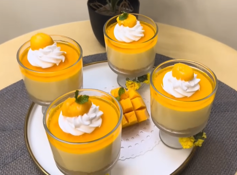 Here's an overhead shot of a no-bake mango cheesecake dessert cup, topped with a swirl of whipped cream and diced mangoes.