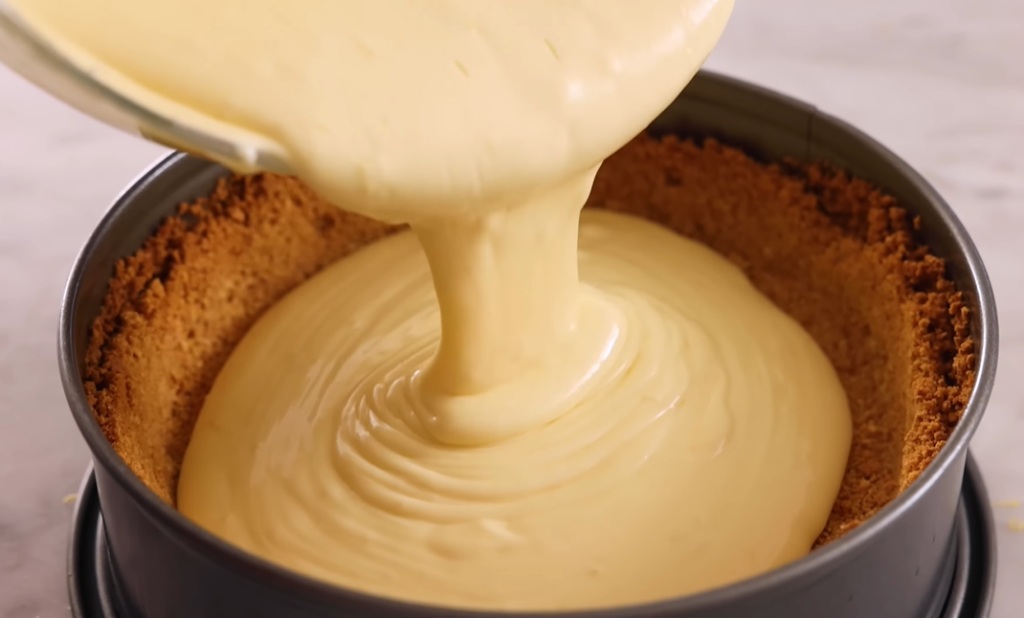 Cheesecake batter being poured into a springform pan with a pre-baked crust inside.






