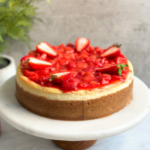 "strawberry cheesecake on a serving stand with strawberry compote and fresh strawberries on top."