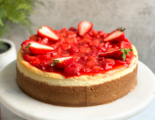 "strawberry cheesecake on a serving stand with strawberry compote and fresh strawberries on top."