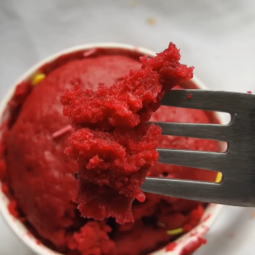 A spoon lifts a moist, fluffy bite, revealing the cake’s soft texture and deep red hue.