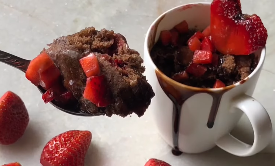 "A decadent chocolate strawberry mug cake with a spoon pulling out a bite, revealing the rich, moist texture inside. The warm chocolate cake is perfectly complemented by fresh strawberries, offering a satisfying indulgence in every spoonful."