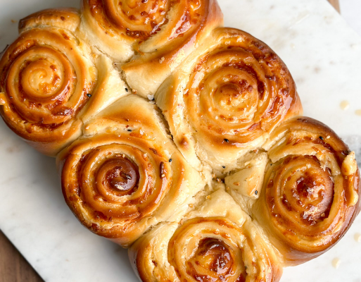 Six freshly baked cheesy bread rolls in a line on a serving board, featuring a rich golden color and a drizzle of honey butter on top.