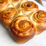 Six freshly baked cheesy bread rolls in a line on a serving board, featuring a rich golden color and a drizzle of honey butter on top.