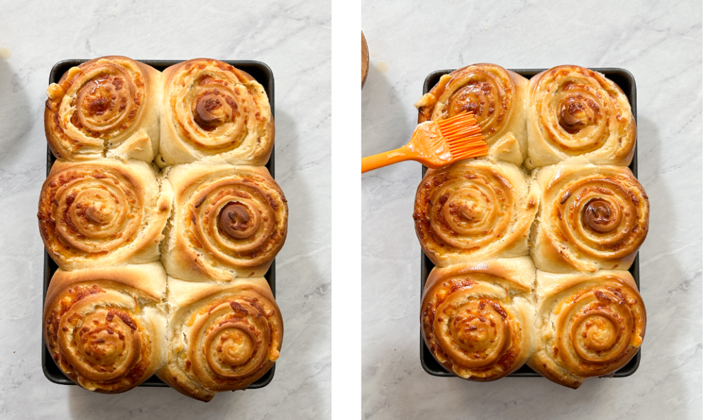 A pastry brush applying a golden honey butter glaze onto freshly baked cheesy bread rolls. This adds a rich, sweet finish to the warm, fluffy rolls, enhancing their flavor and sheen.